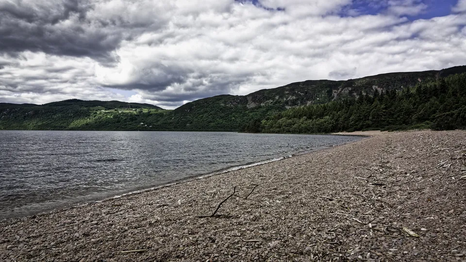 A shingle beach near Tor Point on the north shore of Loch Ness, by Dores, with wooded hills behind