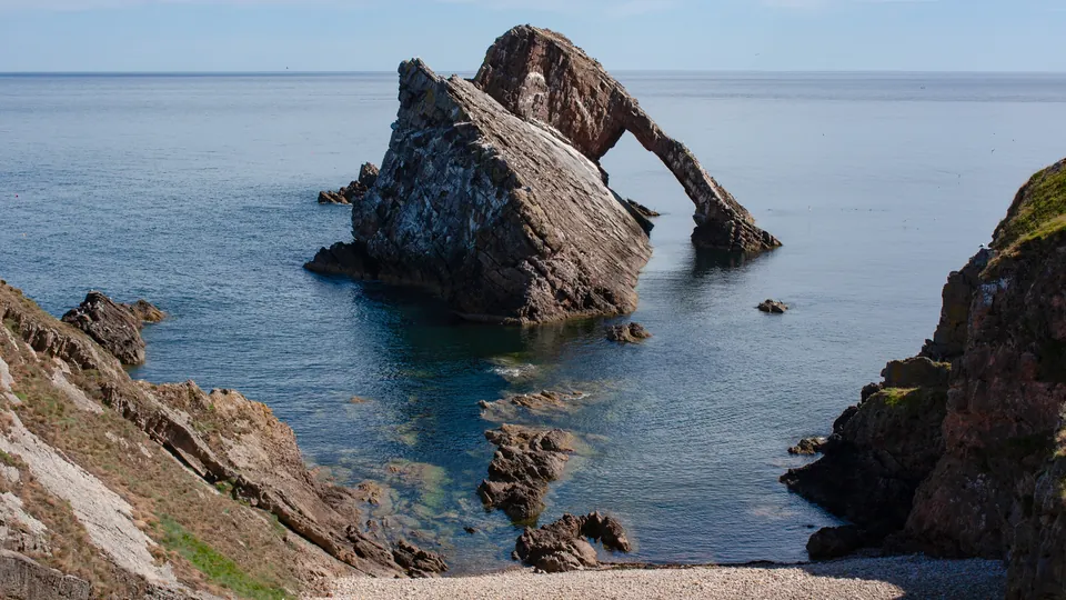 Bow Fiddle Rock, a sea arch off the cliffs at Portknockie on the Moray coast, seen from a pebble cove
